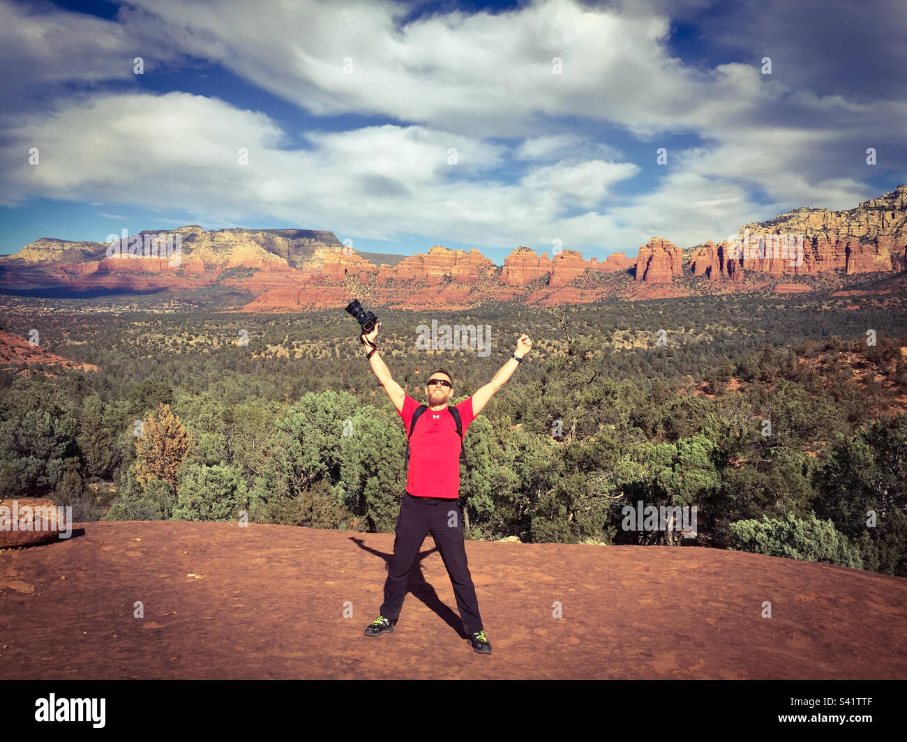 Un uomo con una macchina fotografica tiene le braccia in alto nel deserto a Sedona Arizona - Immagine stock catturata con smartphone