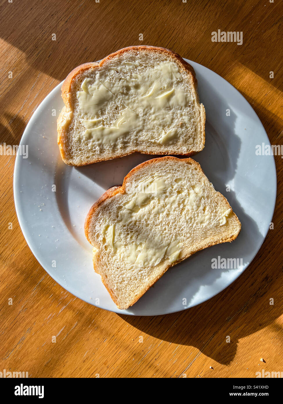 Due fette di pane bianco imburrato a fette su piatto bianco Foto Stock