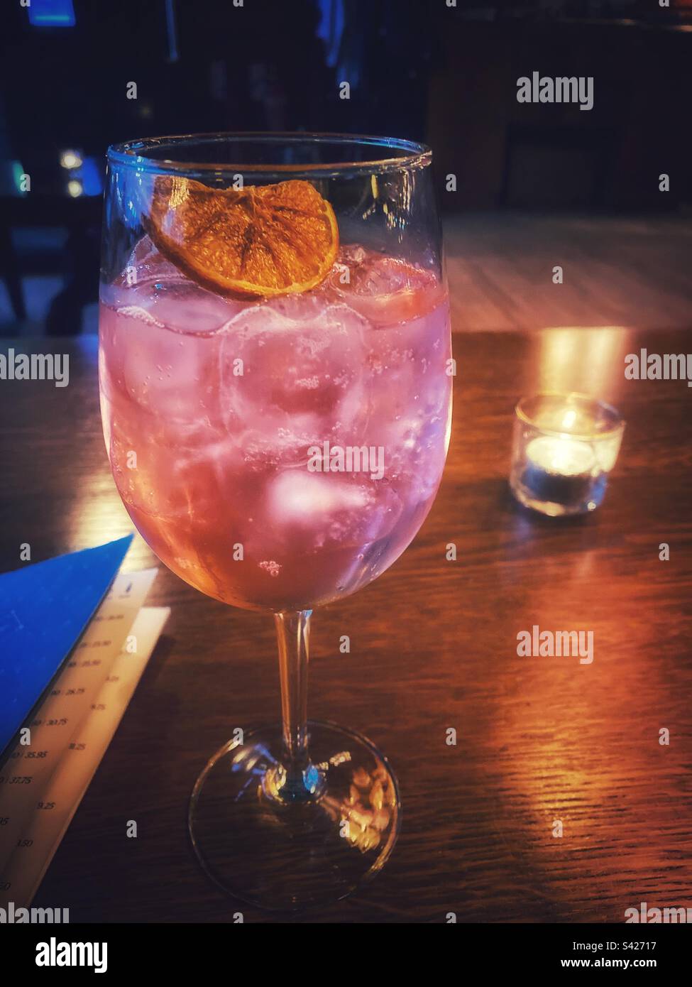 Una fotografia di un cocktail in un bicchiere di vino al bar, con una candela accesa. Foto Stock