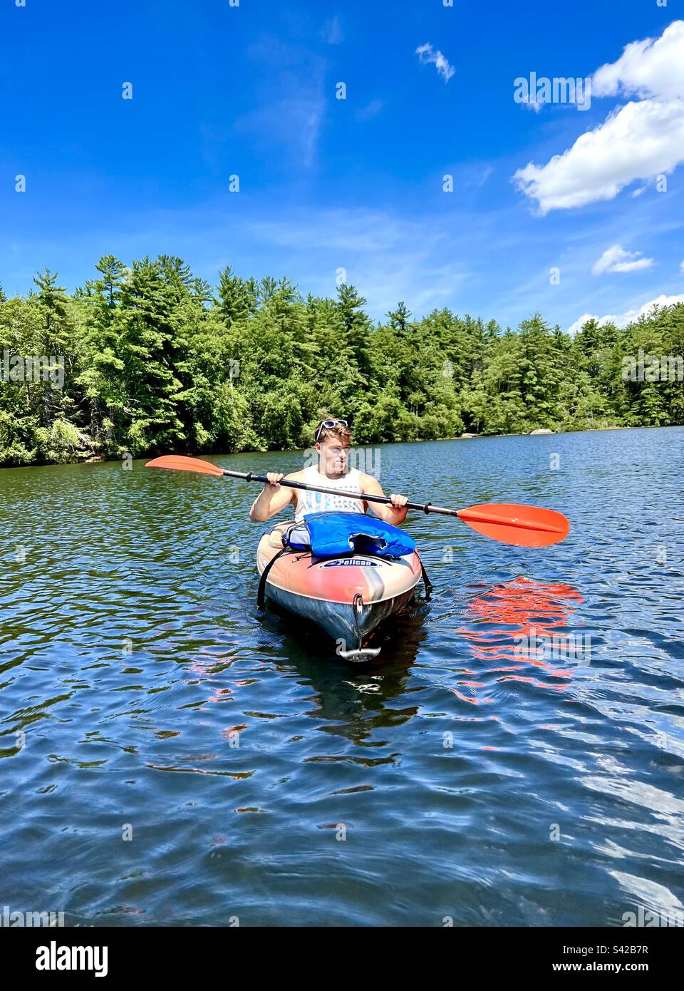 Un maschio giovane e fisicamente in forma che va in kayak sul lago Pawtuckaway nel New Hampshire in una calda e soleggiata giornata estiva - Immagine stock catturata con smartphone