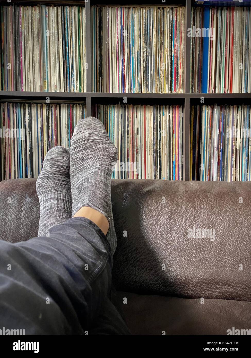 Una grande collezione di dischi in vinile copertine su scaffali uomo seduto con gambe incrociate sul divano in pelle Foto Stock