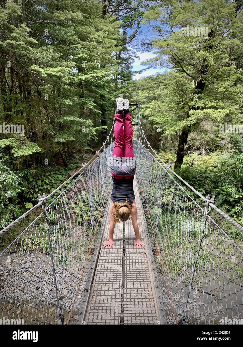 Una donna atletica che fa un cavalletto su un alto ponte di corda sul Kepler Walk a Manapouri vicino te Anau, nell'Isola del Sud Nuova Zelanda Foto Stock