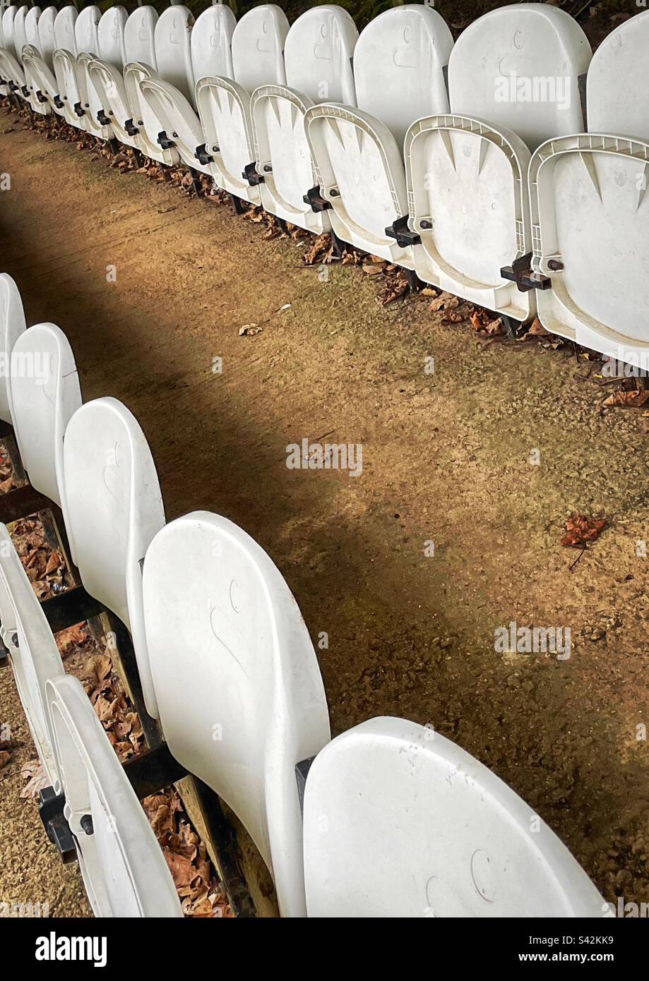 Le foglie autunnali giacciono a terra sotto i sedili in plastica bianca di un campo da calcio semi-professionale. Foto Stock