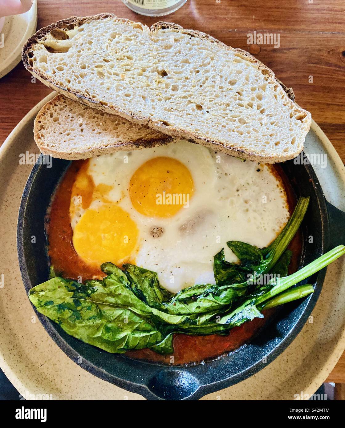 Fuoco uova arrosto con verdi su un letto di fagioli con pane tostato con pasta madre. - Immagine stock catturata con smartphone