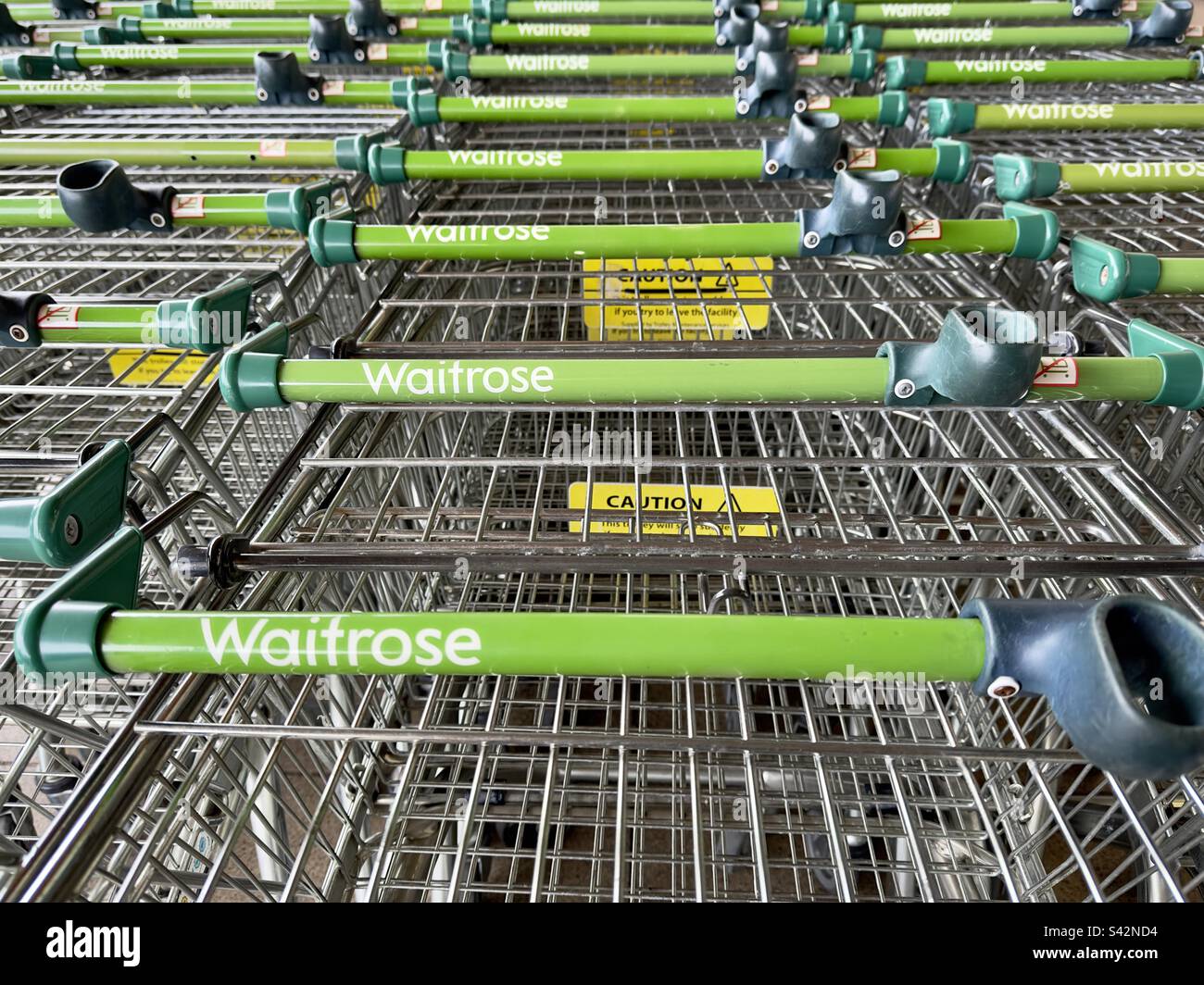 Le maniglie di lunghe file di carrelli vuoti per supermercati, in attesa all'esterno del negozio e recante il logo Waitrose. - Immagine stock catturata con smartphone