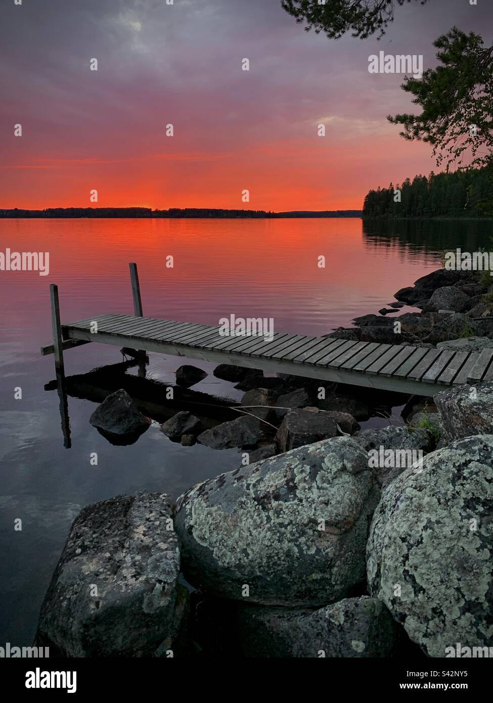 Sole di mezzanotte e un cielo rosso sangue su un molo del lago in una casa estiva nella regione di Kajaani in Finlandia Foto Stock