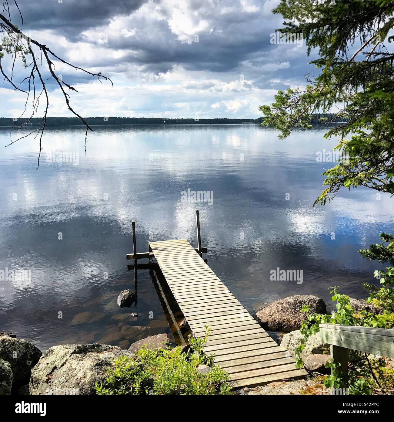 Durante un'estate artica, le nuvole di tempesta oscure si riflettono in un grande lago presso un molo estivo nella regione finlandese di Kajaani Foto Stock