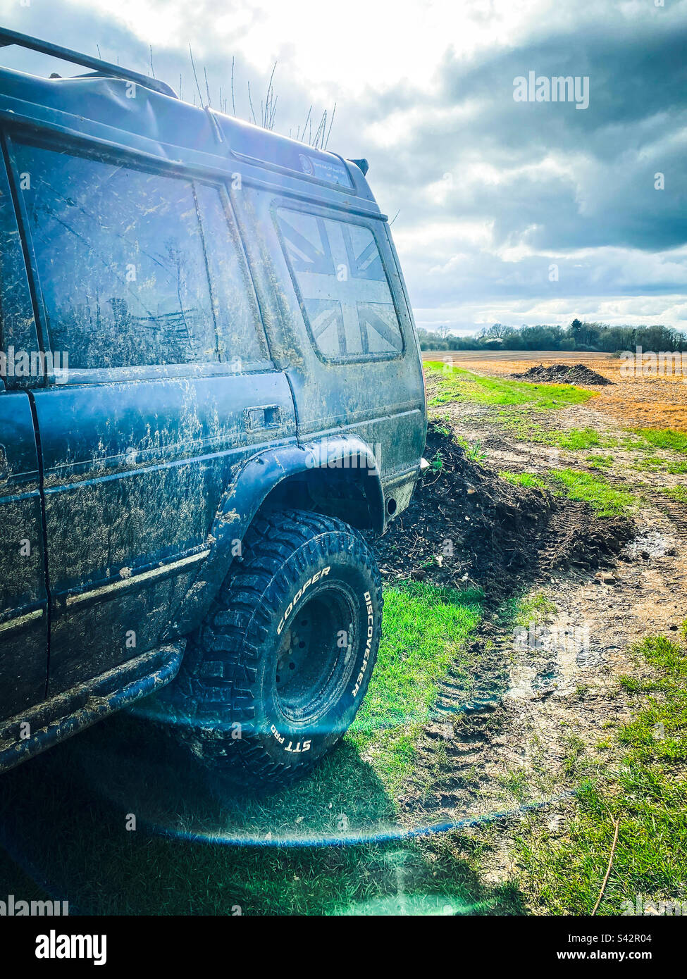 Un veicolo fuoristrada è parcheggiato in campagna da un campo fangoso - Immagine stock catturata con smartphone