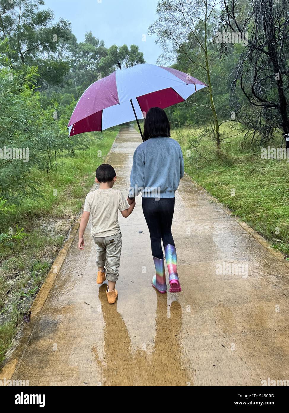 Fratello e sorella camminano sotto la pioggia sotto un ombrello Foto Stock