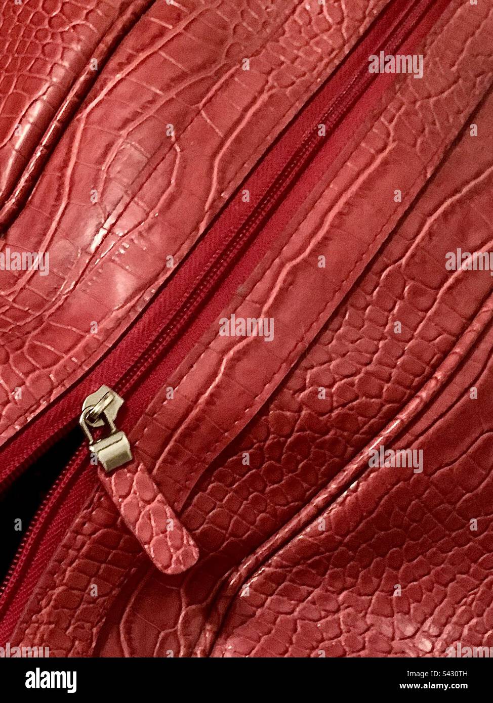 Primo piano di borsone in pelle rossa con texture in pelle di serpente sintetica, la cerniera si apre parzialmente nell'angolo inferiore - Immagine stock catturata con smartphone