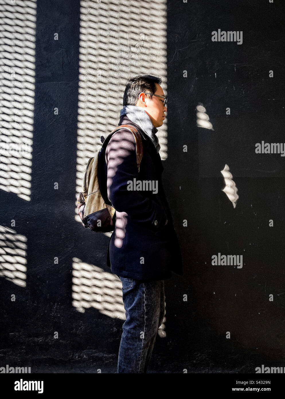 Foto di tre quarti di lunghezza della vista laterale del giovane uomo in piedi contro la parete modellata d'ombra. Foto Stock