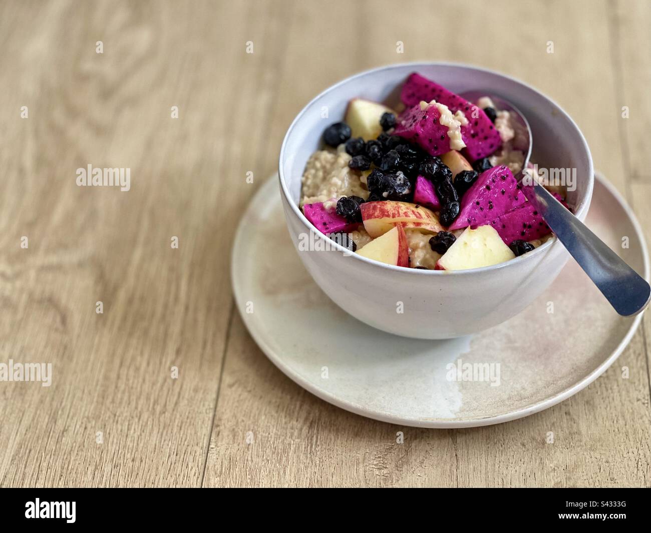 Vista dall'alto della farina d'avena con frutta fresca a fette e mirtilli secchi in una ciotola con cucchiaio su piatto su tavolo di legno. Foto Stock