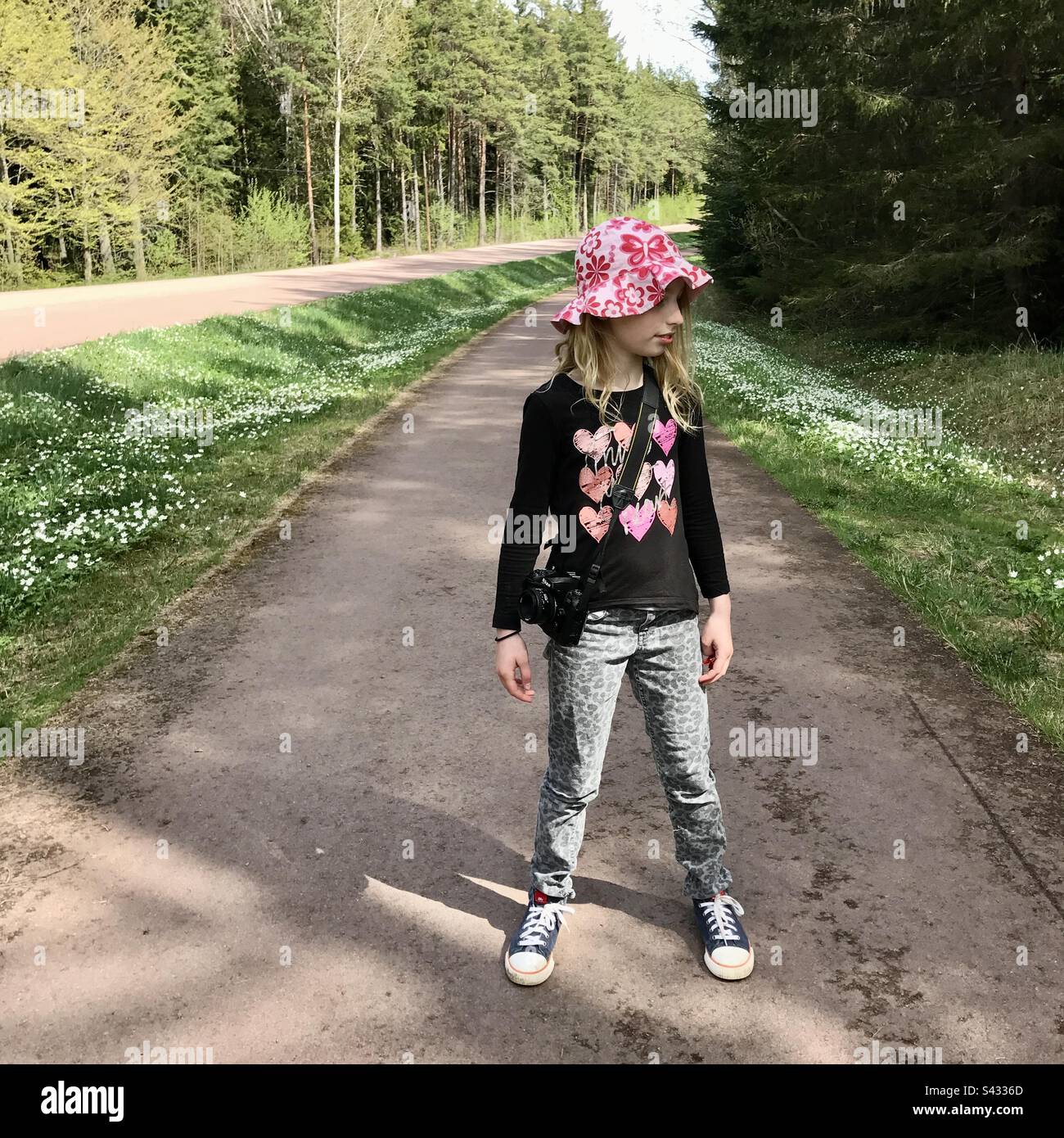 Giovane bambina di 8 anni che cammina su un percorso fiancheggiato da fiori primaverili attraverso una foresta nella bella luce del sole primaverile Foto Stock