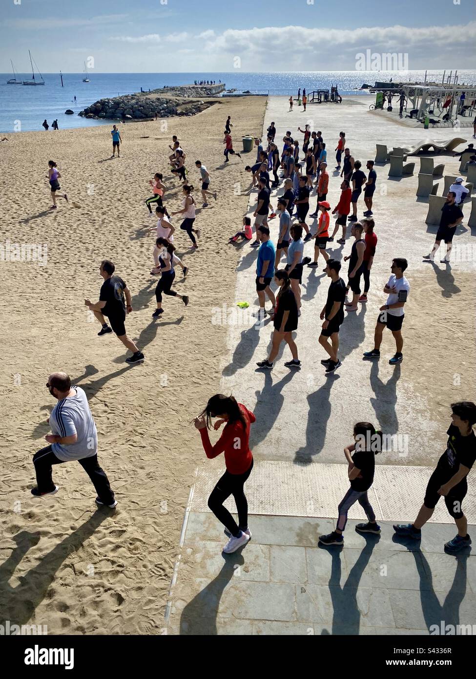 Un gruppo di persone di tutte le età che fanno l'esercizio mattutino di intervalli e sprint sulla trafficata spiaggia della città di Barceloneta a Barcellona, Spagna Foto Stock