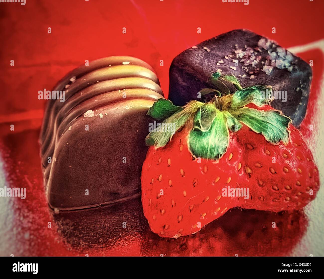 Primo piano di fragola fusa, cioccolato fondente salato e cioccolato al miele pralina su sfondo rosso riflettente. Foto Stock