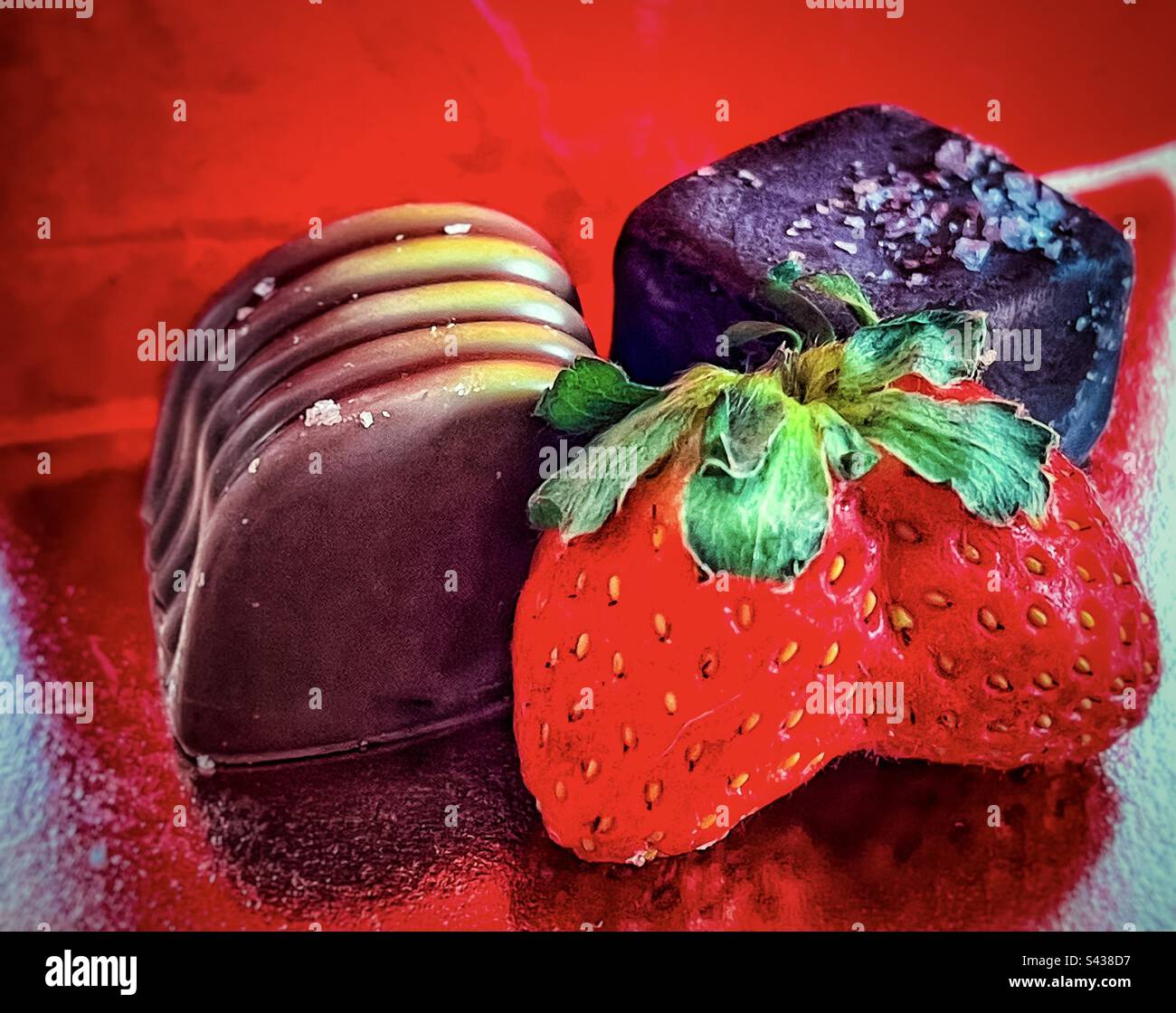 Primo piano di fragola fusa, cioccolato fondente salato e cioccolato al miele pralina su sfondo rosso riflettente. Foto Stock