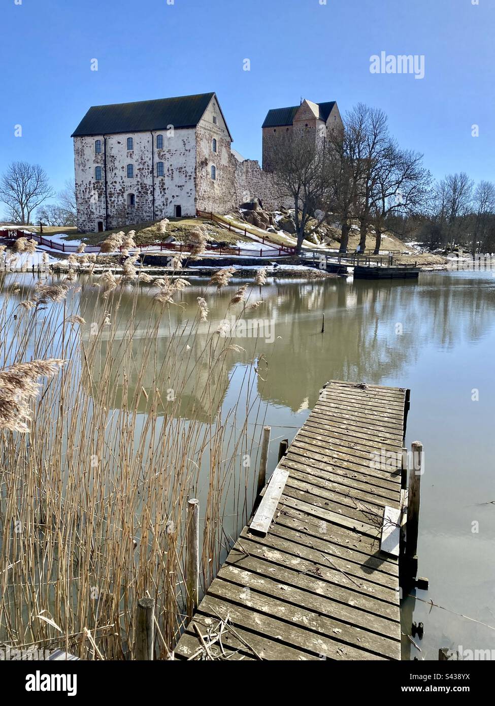 Il bellissimo castello antico di Kastelholm nell'arcipelago delle isole Åland, nella regione del Mar Baltico in Finlandia, con l'inverno che si trasforma in primavera. Vista su un molo in decadenza su un lago marino interno. Foto Stock