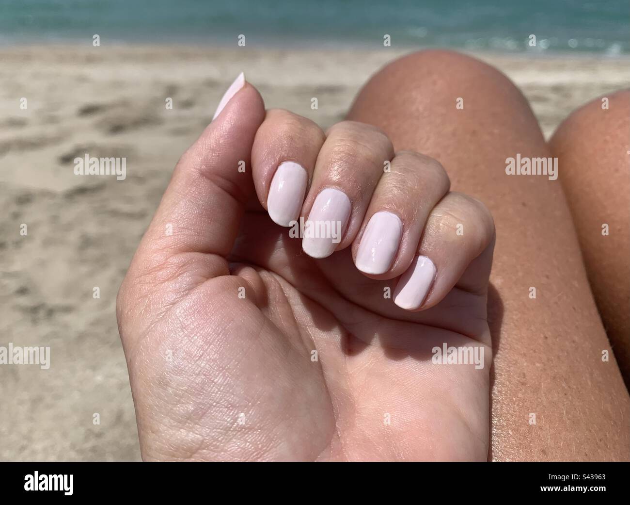 Mano di donna con unghie rosa pallido appena curate su fondo di sabbia e mare - Immagine stock catturata con smartphone