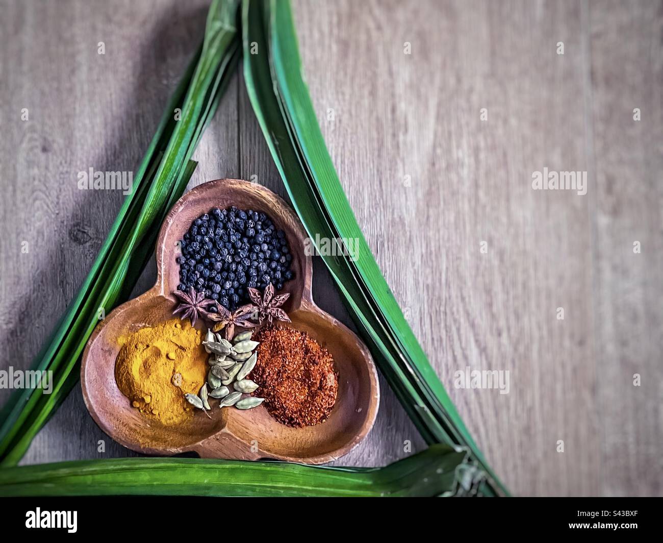 Direttamente sopra la foto di spezie asiatiche colorate disposte in una ciotola decorativa di legno incorniciata da foglie verdi di Pandano, note anche come pandan o foglie di pino a vite su legno con spazio copia. - Immagine stock catturata con smartphone