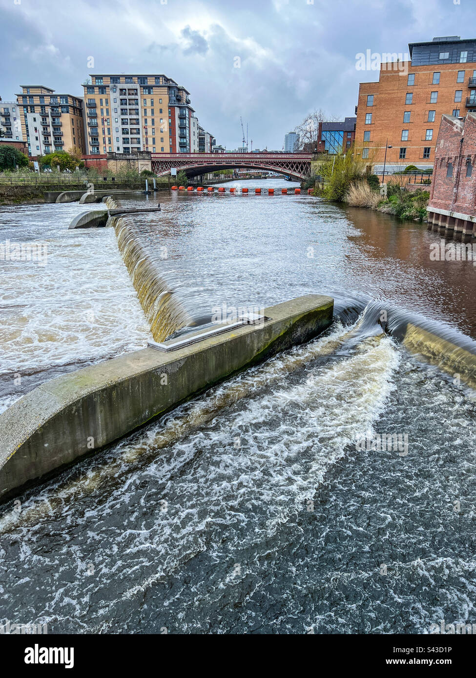 Fiume che scorre attraverso Leeds con ponte weir braccio arancione e flusso eccessivo Foto Stock