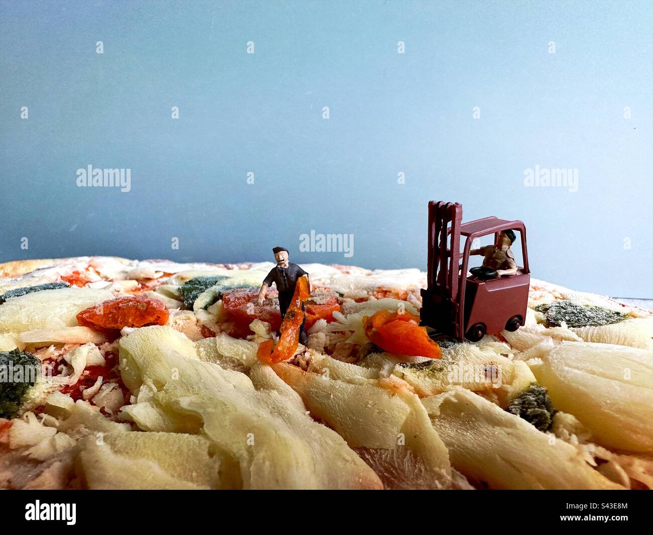 Persone in miniatura che mettono un condimento su una pizza Foto Stock