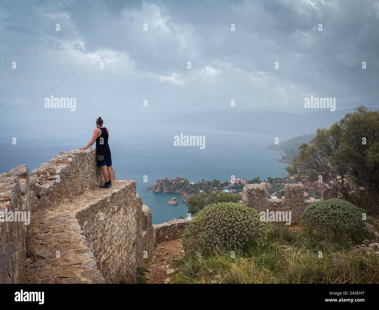 L'uomo gode di una vista incredibile dalla cima di antiche mura in pietra, Rocca di Cefalù, Sicilia. Foto Stock