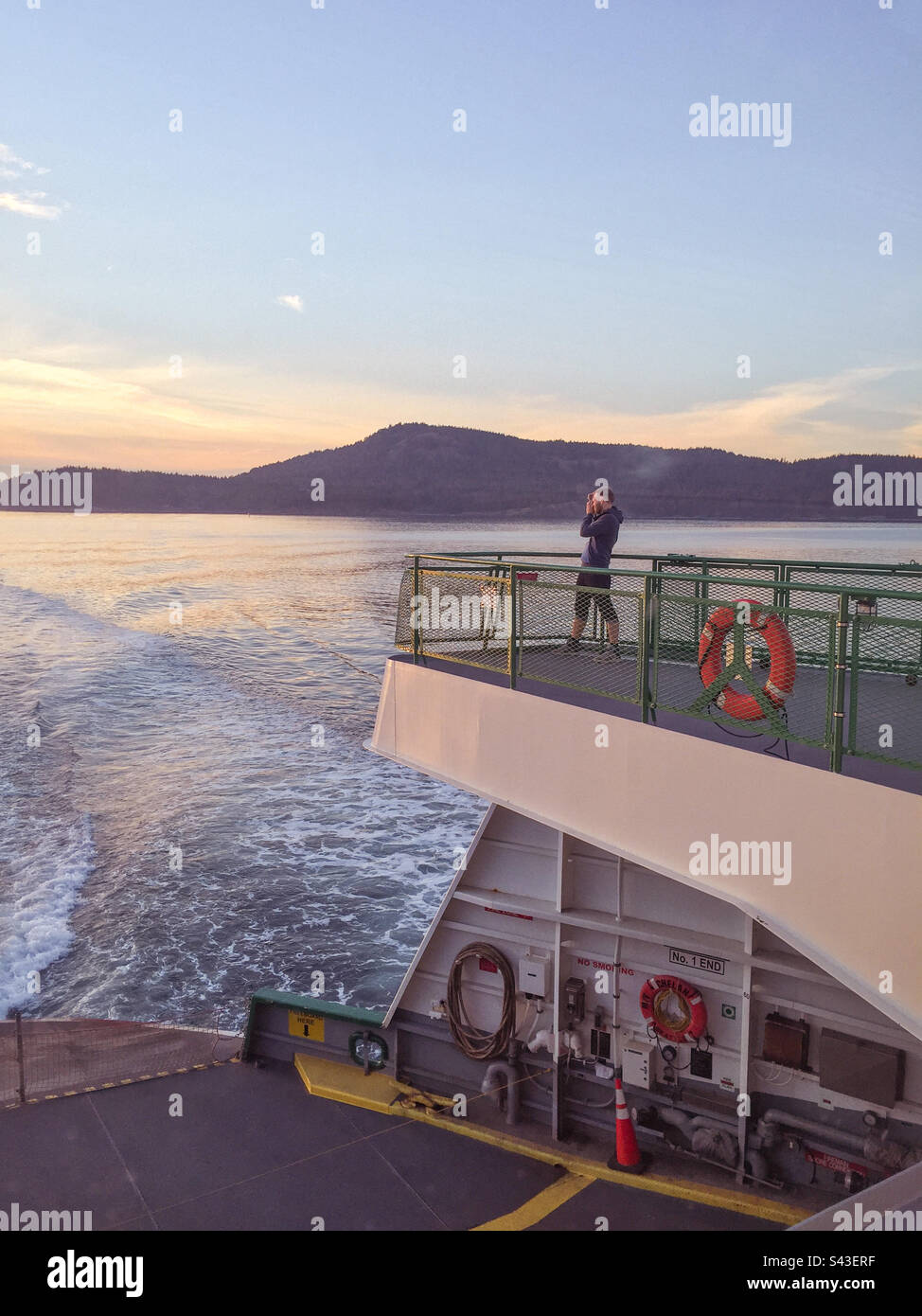 Uomo che scatta foto di un bellissimo tramonto sul retro di un traghetto nel Puget Sound, Washington state, USA. - Immagine stock catturata con smartphone