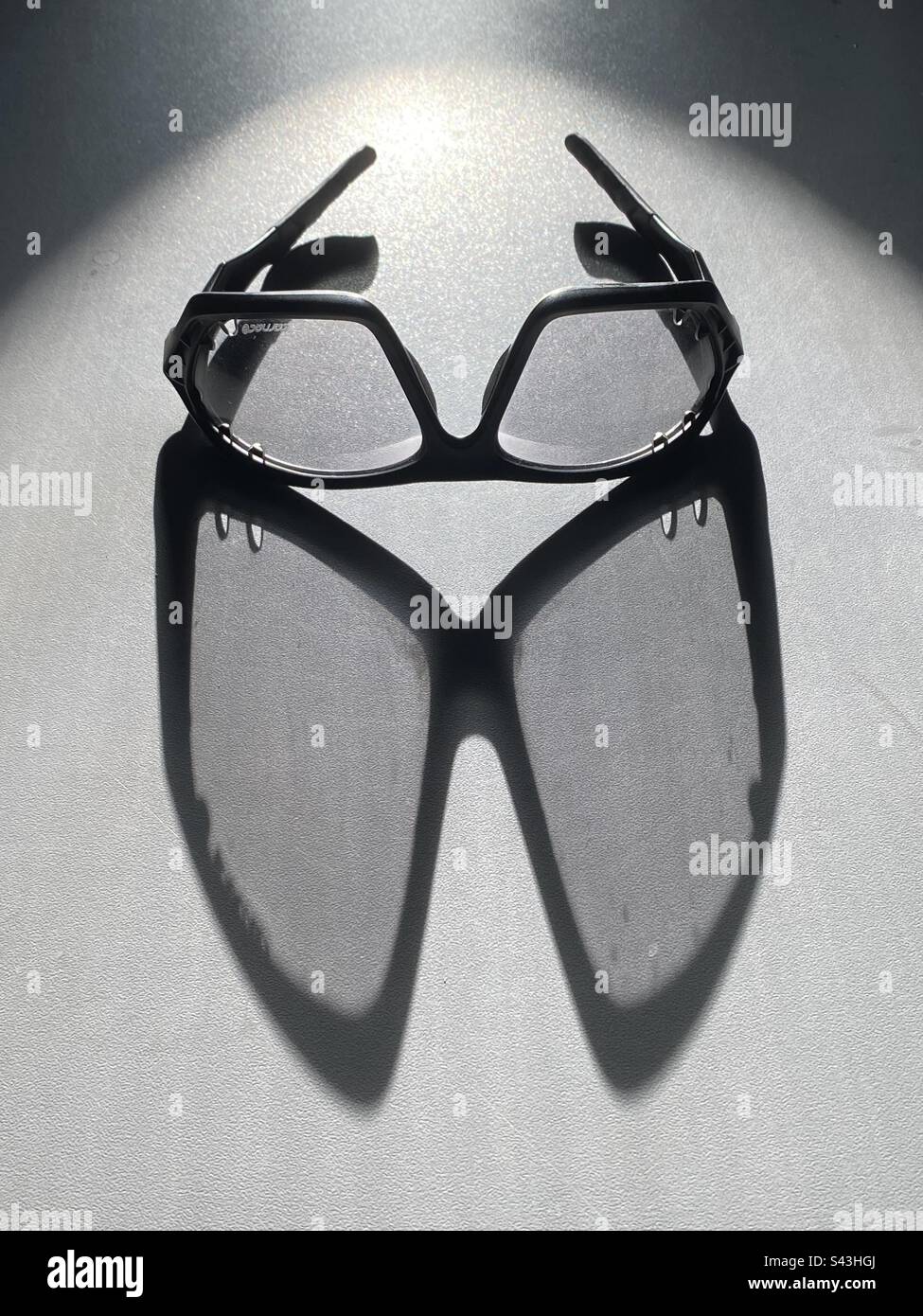 Un paio di occhiali da bicicletta gettano un'ombra su un piano di un bancone alla luce del sole Foto Stock