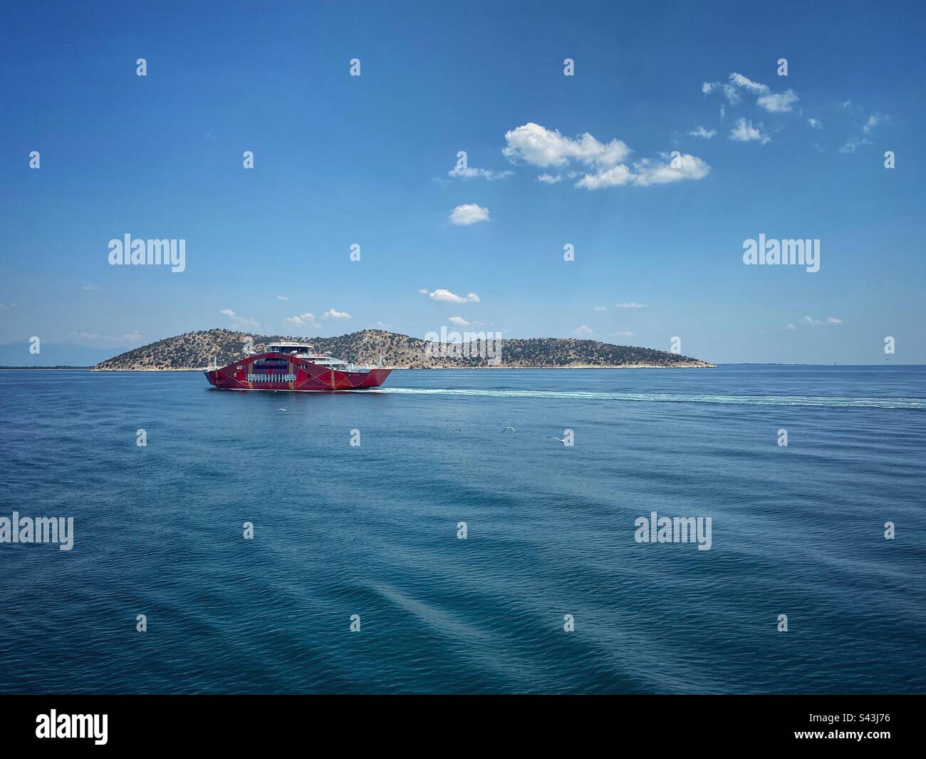 Vista sul mare con l'isola di Thassopoula e un traghetto rosso che naviga verso l'isola di Thassos in Grecia. Foto Stock