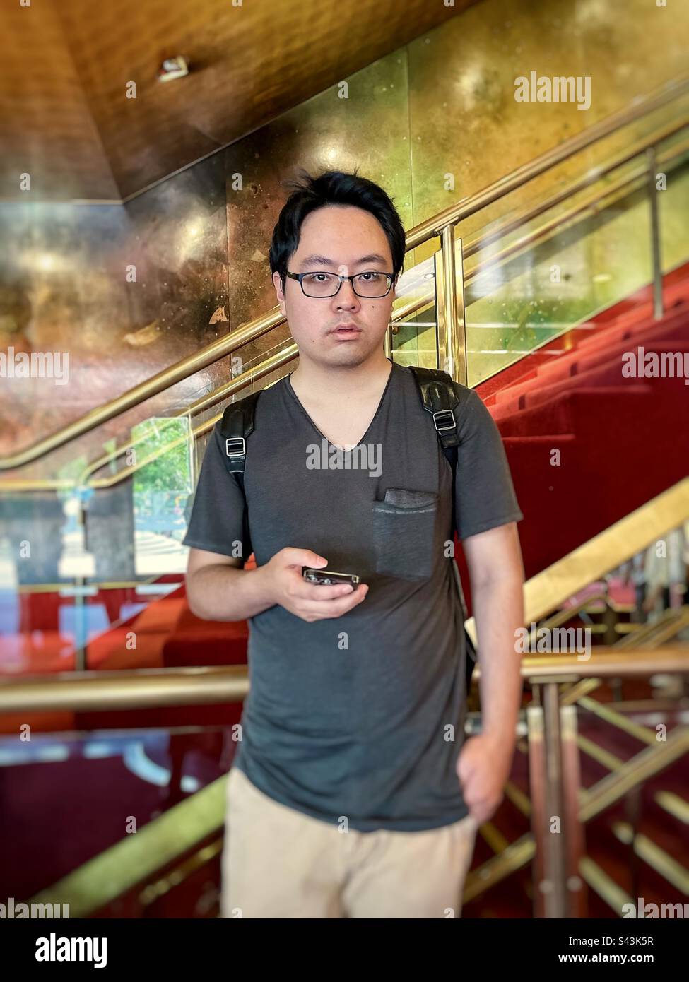 Giovane asiatico che usa il telefono a mano contro le scale e le ringhiere. - Immagine stock catturata con smartphone