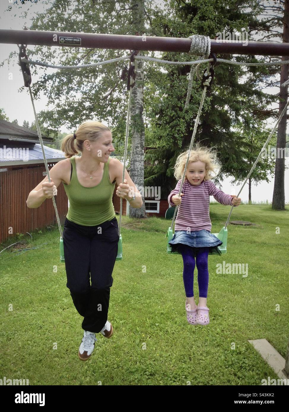 Ragazza giovane figlia di 4 anni sorridente su un parco giochi swing in vacanza in estate con la madre Foto Stock