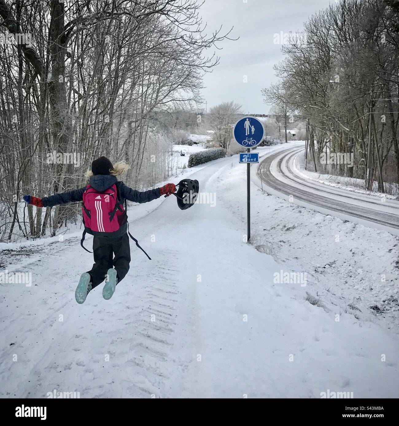 Una giovane ragazza di 10 anni che salta con gioia su un sentiero pubblico sulla strada per la scuola nel profondo inverno in Scandinavia Foto Stock