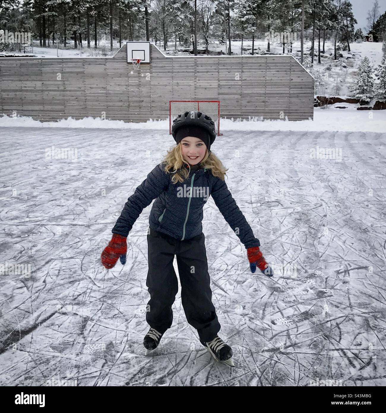 Una giovane ragazza di 10 anni in un casco pattinaggio su ghiaccio su una pista di pattinaggio pubblica nel profondo inverno in Scandinavia Foto Stock