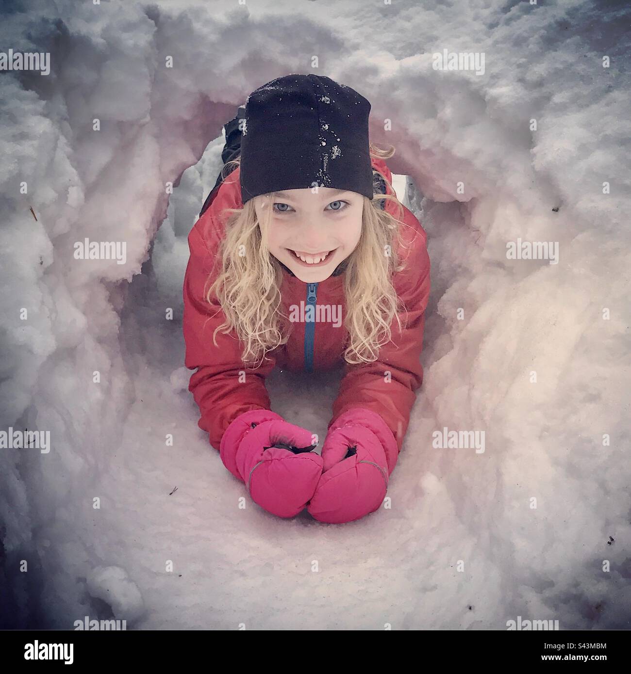 Una giovane ragazza di 10 anni sorridente che striscia attraverso un tunnel di neve in inverno profondo in Scandinavia Foto Stock