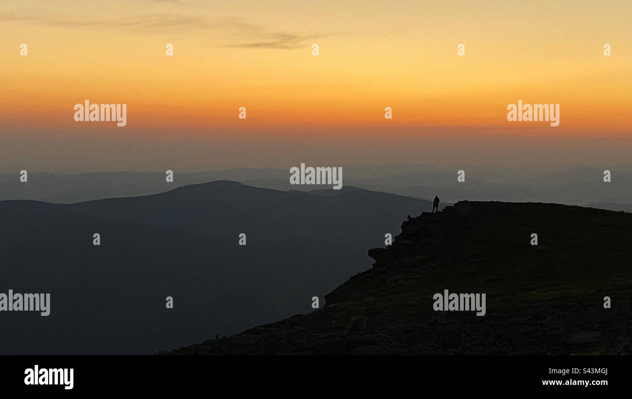 Uomo che guarda l'alba. Montagne all'alba. Uomo in piedi sul picco. Paesaggio montano naturale con cime nebbiose illuminate, pendici nebbie e valli - Immagine stock catturata con smartphone