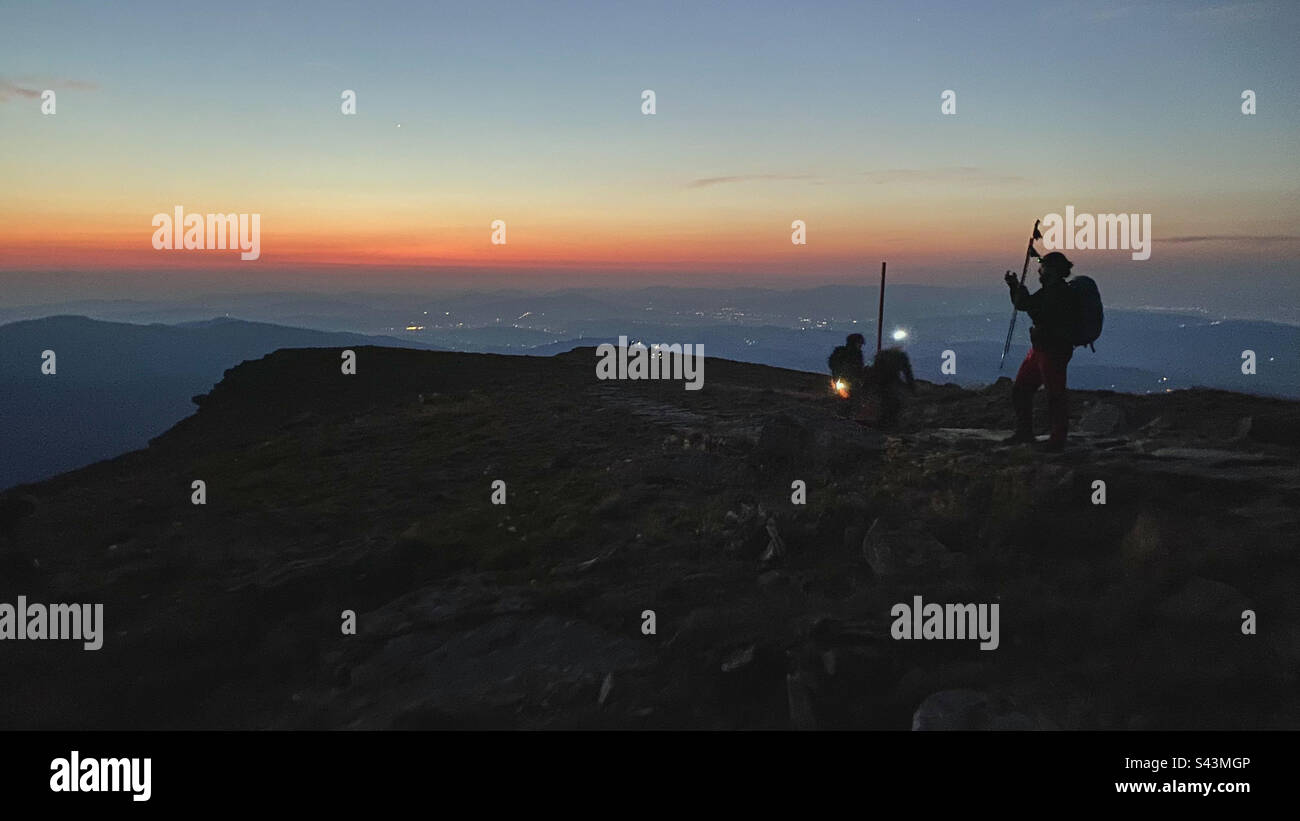 Persone che camminano di notte. Montagne all'alba. Uomo in piedi sul picco. Paesaggio montano naturale con cime nebbiose illuminate, pendici nebbie e valli - Immagine stock catturata con smartphone