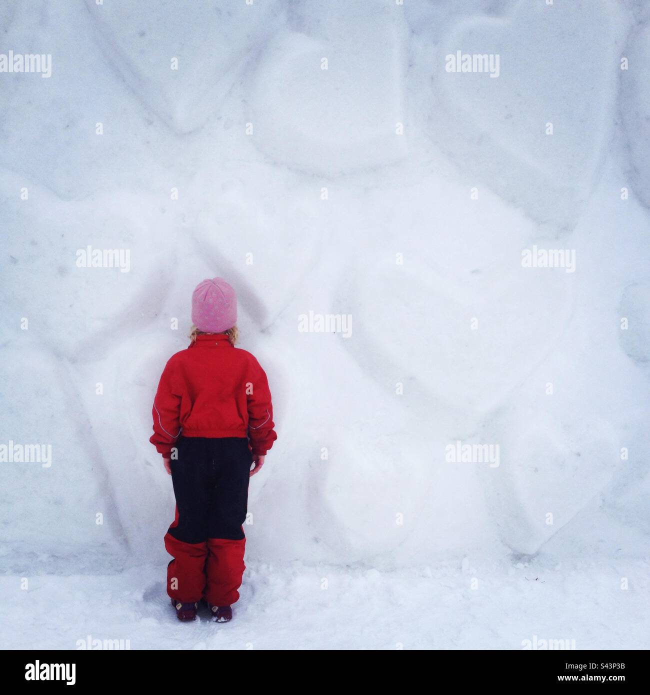 Una giovane ragazza di 6 anni di fronte ad una parete del cuore di neve in un parco giochi pubblico che gioca a nascondino e cerca nel profondo inverno in Scandinavia Foto Stock
