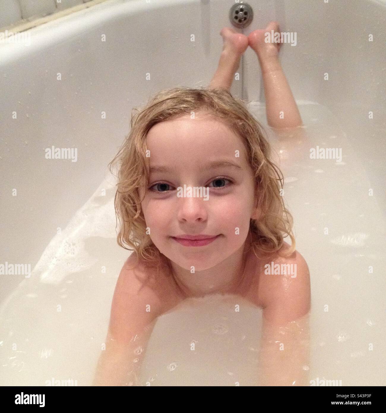 Una giovane ragazza di 6 anni che fa un bagno e che si posa sorridendo alla macchina fotografica Foto Stock