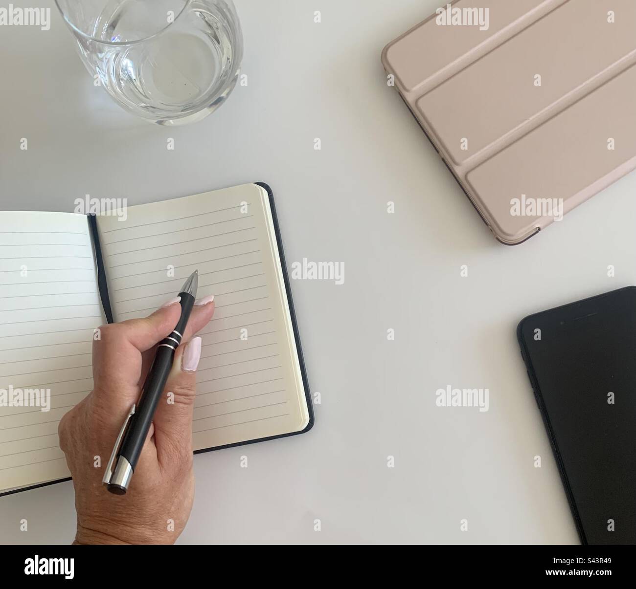 Donna con una penna in mano che prende appunti accanto ai suoi dispositivi elettronici - Immagine stock catturata con smartphone