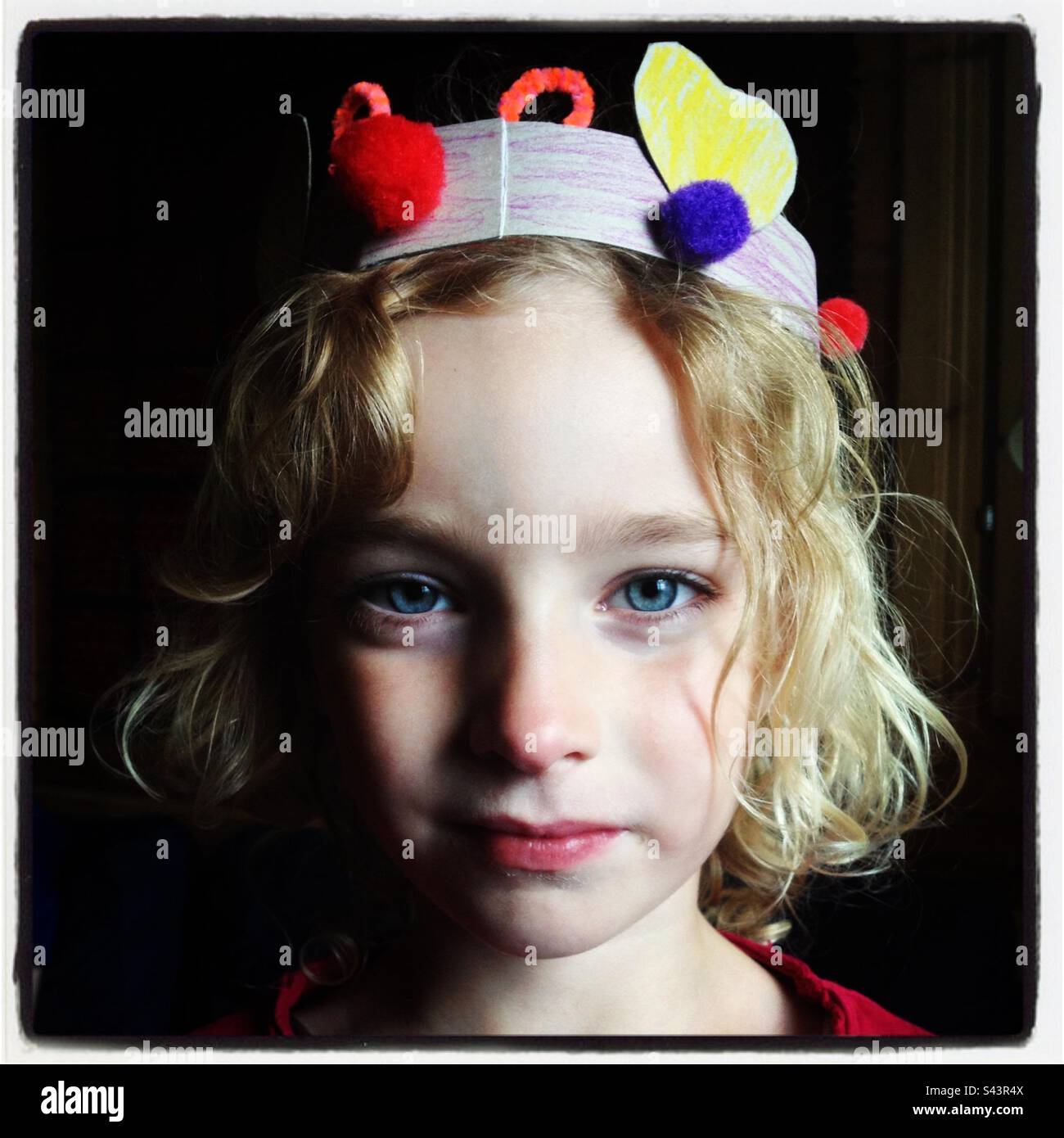 Una giovane ragazza di 5 anni in una casa ha fatto corona di carta che sorride alla macchina fotografica fingendo di essere una regina o una principessa Foto Stock