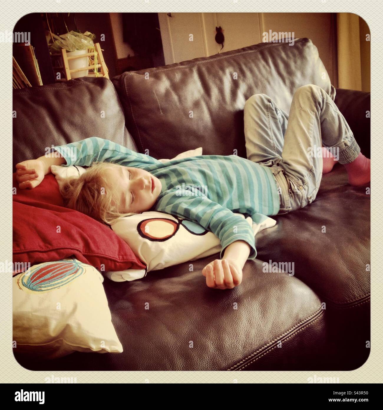 Una giovane ragazza di 6 anni esausta del gioco addormentandosi con una siesta su un divano in pelle a casa nel pomeriggio Foto Stock