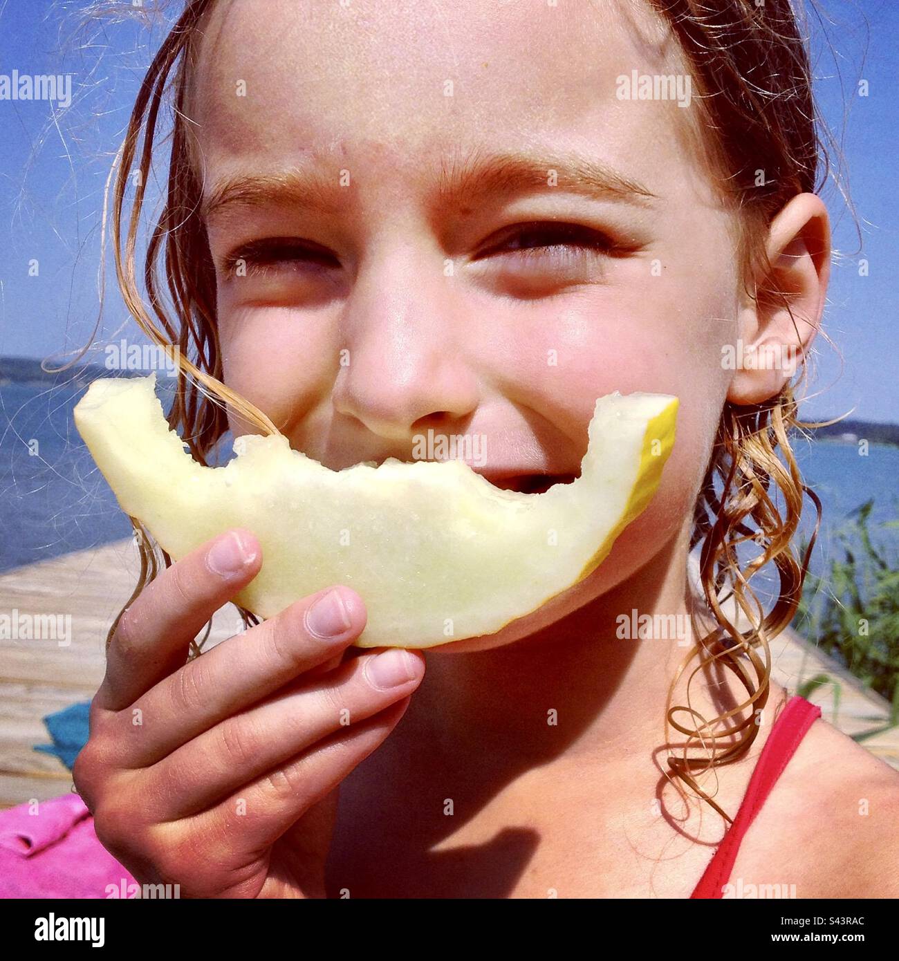 Una giovane ragazza di 6 anni in vacanza che finge di sorridere usando un frutto di melone masticato a forma di bocca Foto Stock