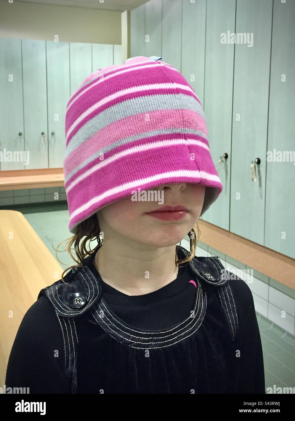 Una giovane ragazza di 6 anni sul dissuasore circa portare il suo cappello rosa sopra il suo volto per un prank Foto Stock