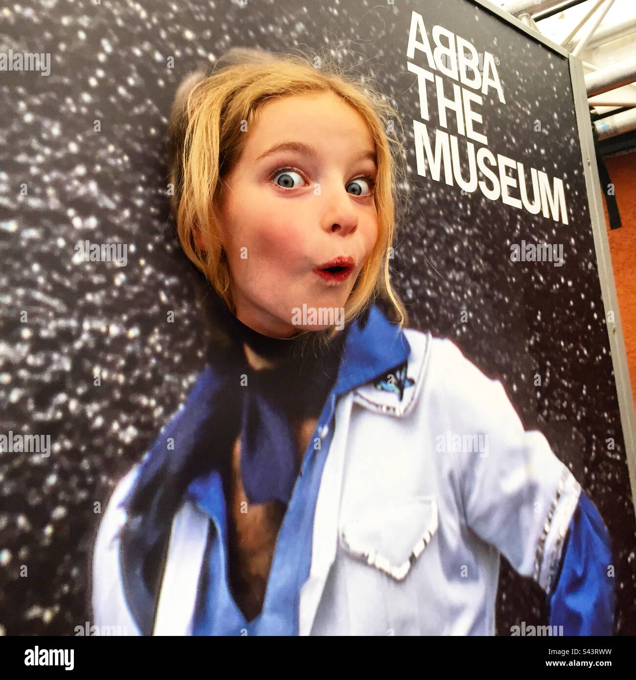 Una giovane ragazza di 7 anni che si scompigliava di posarsi al cartello del Museo Abba di Stoccolma Foto Stock