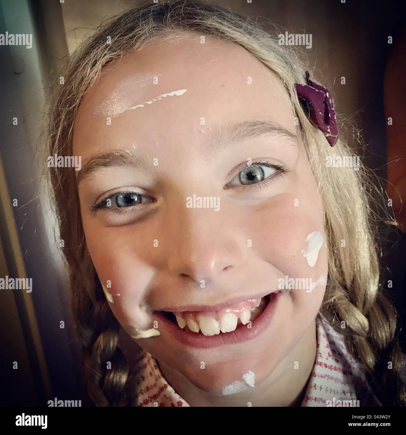 Una ragazza giovane figlia di 9 anni sorridente in estate mettendo crema solare protezione solare sul viso protezione solare vitale per un bambino prima di uscire al sole Foto Stock