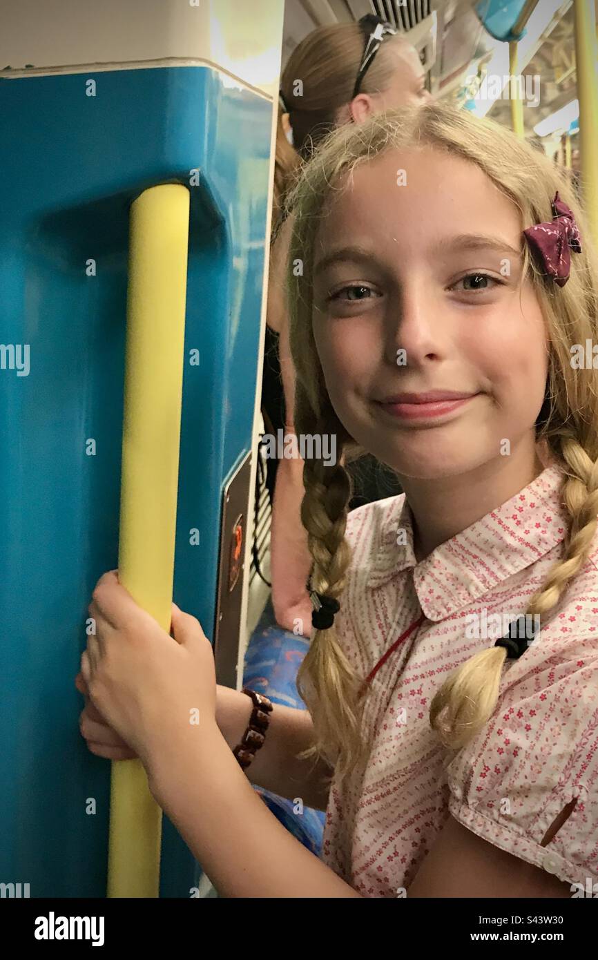 Una bambina di 9 anni, figlia sorridente felice in vacanza in trecce in estate appesa al bar a muro su un treno metropolitano Foto Stock