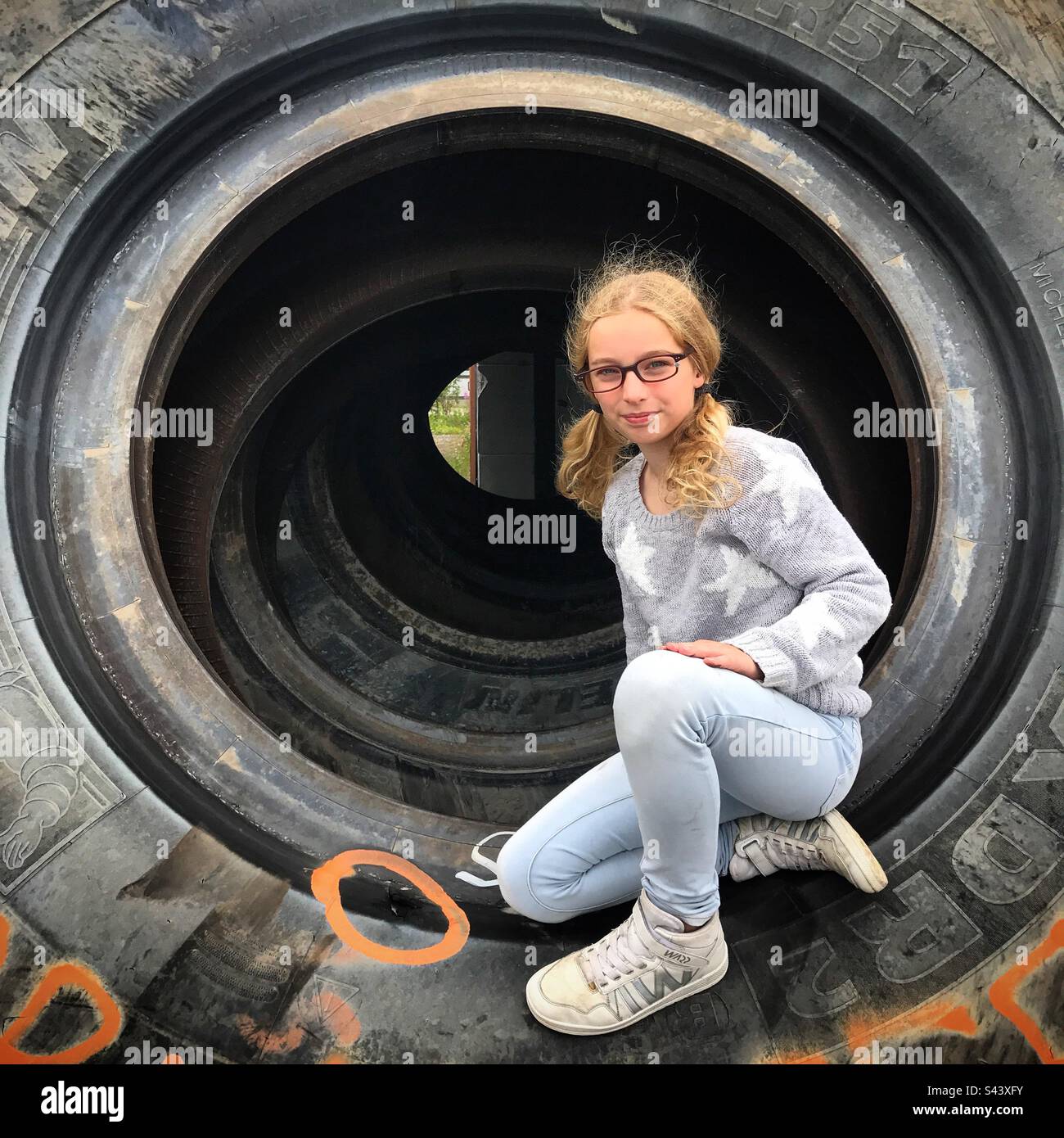 Una ragazza giovane esplorante avventurosa figlia di 9 anni che posa in una gomma gigante con capelli molto ricci crespi e indossare occhiali riparati con un nastro Foto Stock