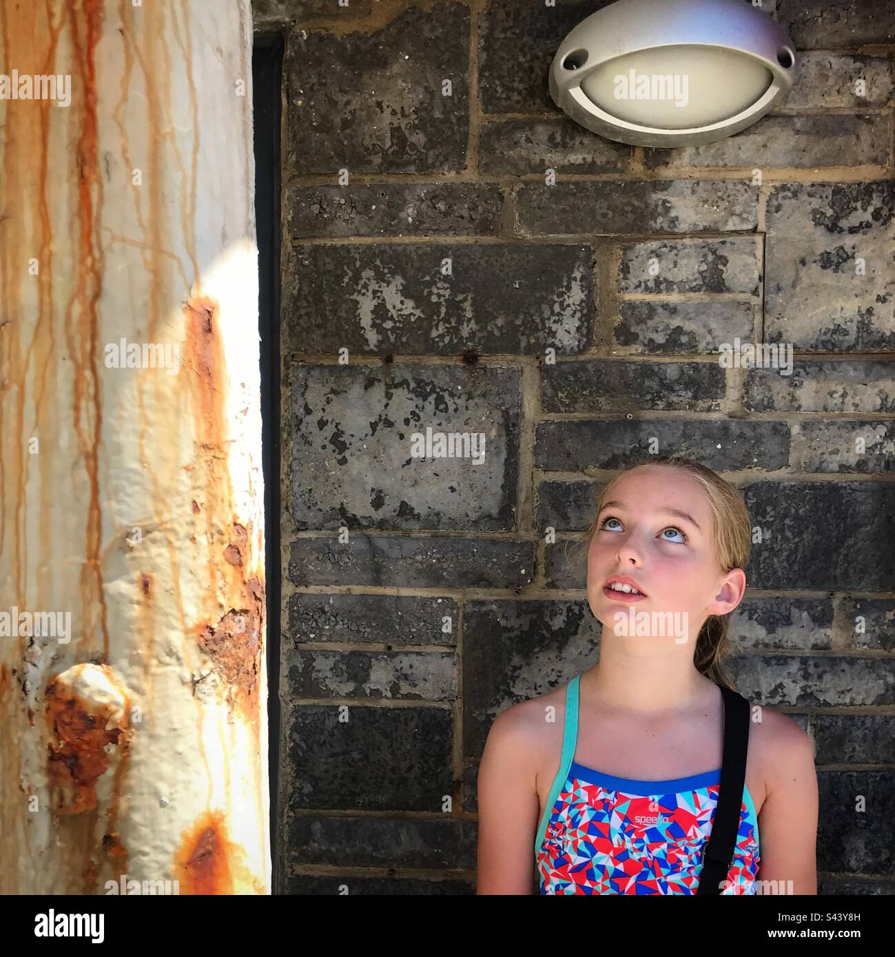 Un ritratto di una bambina di 10 anni in un costume da bagno profondo nel pensiero sognando daydayling fissare simbolicamente su ad una lampada distratto Foto Stock