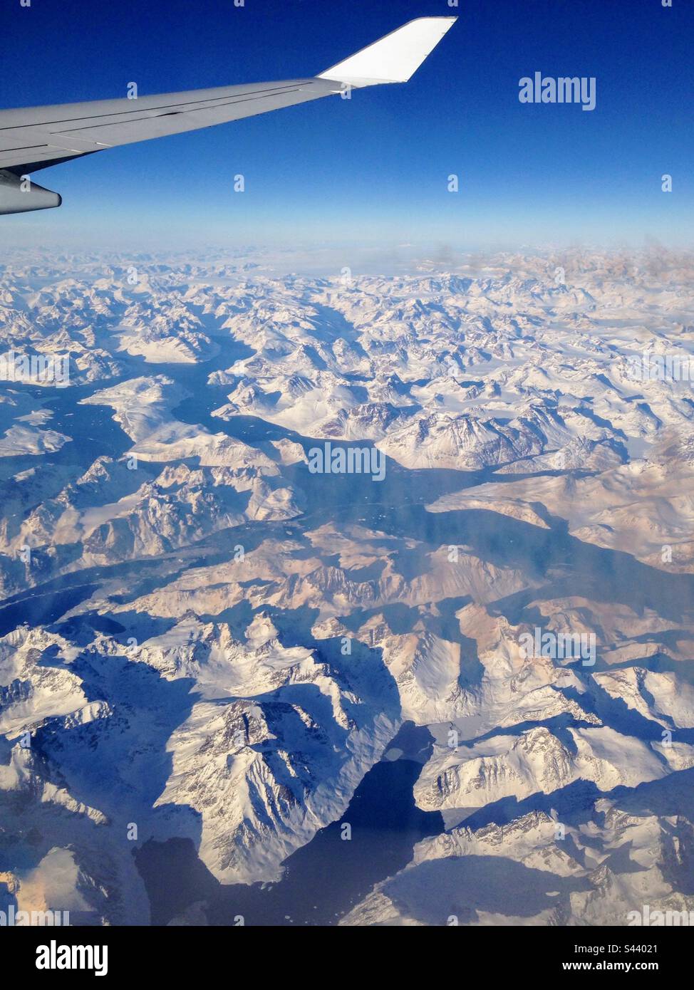 In alto nell'aria: Vista mozzafiato sulle montagne innevate dalla finestra dell'aeroplano - Immagine stock catturata con smartphone