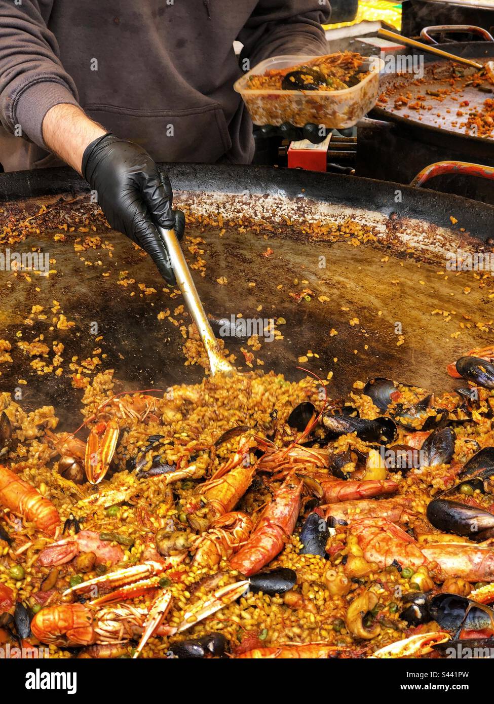 Serve una porzione da una paella in paella cucinare frutti di mare spagnolo paella Street food all'aperto presso il mercato agricolo locale nel Regno Unito - Immagine stock catturata con smartphone